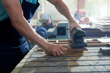 Close-up portrait of strong male hands shaving piece of wood with tool in carpenters workshop making furniture