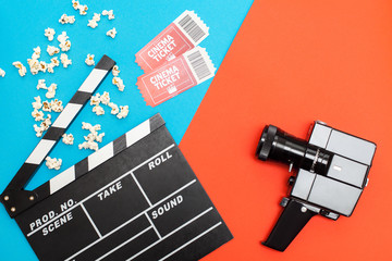 Movie time, flat lay with space for text. Cinema minimal concept. Watching film in the cinema.Top view of popcorn, tickets, movie clapper and retro movie camera on a graphical blue-orange background