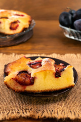 Piece of plum cake on a round plate, linen napkin, vertical frame, wooden background.