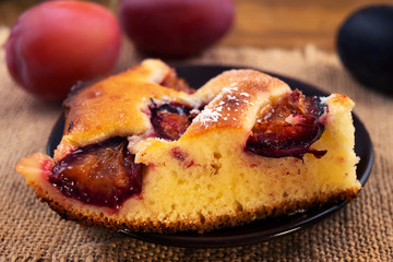 A portion of the pie with plums on a round plate on the background of ripe plums purple and blue, close-up.