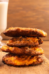 Homemade cookies stacked on top of each other on a linen napkin, vertical frame, wooden background, milk in a glass in the background.