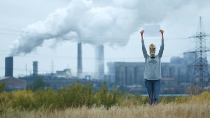 Woman in a gas mask on a background of smoky pipes of a factory