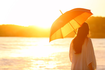 Woman with umbrella at sunset on the beach