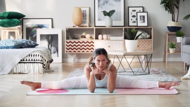 Beautiful slim woman in thirties with fair complexion does splits on mat in modern airy room with fair sophisticated interior in Scandinavian style