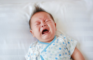 Portrait of infant baby boy crying and screaming lying on bed.