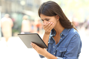 Worried girl reading online news in a tablet