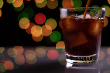 Glass With Ice And Coffee Poured Into It On A Shiney Platform With Dark Background And Colorful Bokeh Lights