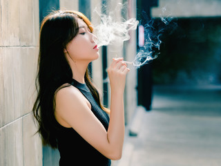 Portrait of beautiful Chinese girl smoking outdoor and thinking about problems, seems a little bit lost, in vintage mode.