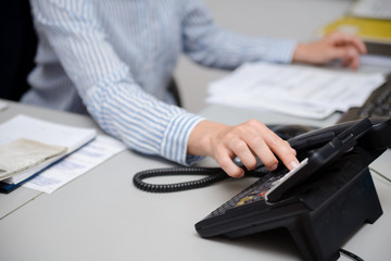 Closeup of businesswoman dialing making office phonecall, light table background. Corporate female holding telephone handle digital electronic pc connection checking daily data news, online talk job.