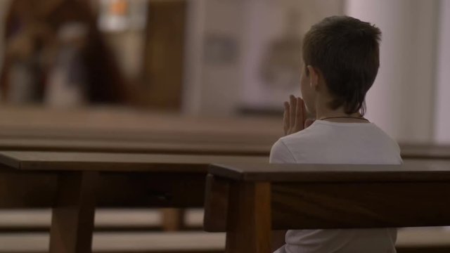 serious boy praying in the Church alone, back view