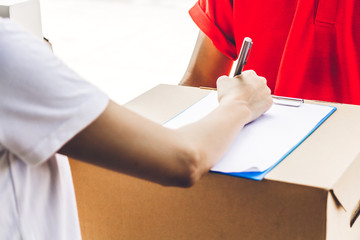 Woman putting signature in clipboard on cardboard box with delivery man.courier service concept