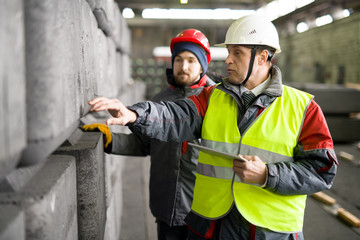 Waist up portrait of mature worker  wearing warm jacket and hardhat using digital tablet while...