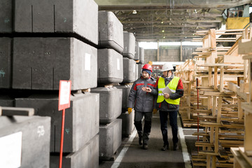 Full length portrait of mature foreman wearing hardhat  discussing manufacturing with worker while...