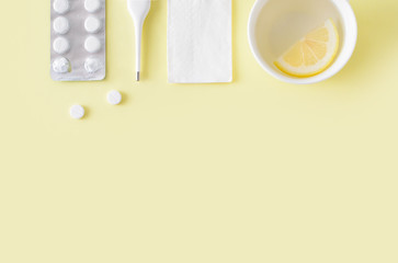 Pills, thermometer and cup of tea on yellow background. Cold and flu treatment set. Flat lay, top view. Free copy space.