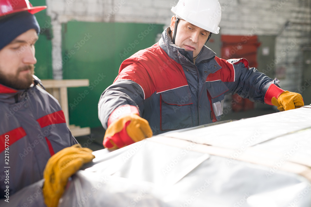 Wall mural Portrait of mature factory worker wearing hardhat packaging shipment units in industrial workshop, copy space