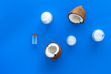 Coconut oil cosmetics for skin and hair care. Oil in small bottle, cream jar, halfs of coconut with shelf on blue background top view space for text