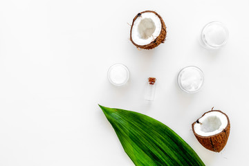 Coconut oil cosmetics for skin and hair care. Oil in small bottle, cream jar, halfs of coconut with shelf, palm leaves on white background top view copy space