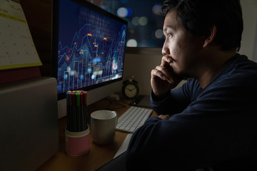 Portrait of Asia Businessman sitting and working hard on the table with Trading graph on the cityscape over front of computer screen in work place at late with serious action