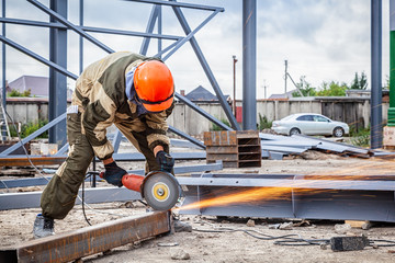A strong  man welder in brown uniform, a construction helmet and welders leathers, grinder metal an...