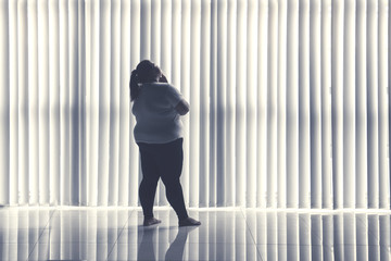 Fototapeta na wymiar Pensive obese woman stands by the window