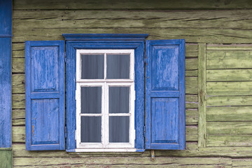 old weathered white window with blue shutters on green wooden wall