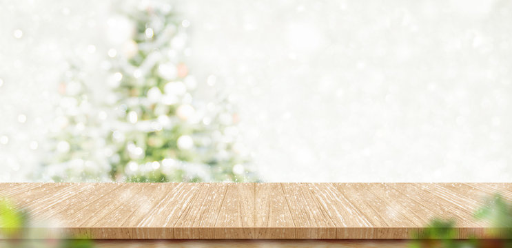 Empty brown wooden table top with abstract muted blur christmas tree and snow fall background with bokeh light,Holiday backdrop,Mock up banner for display or montage of product.