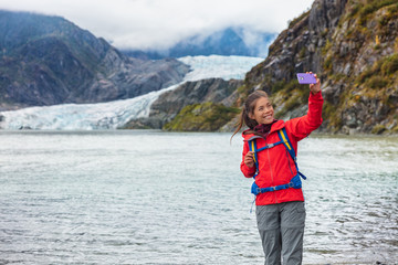 Tourist woman taking selfie photo at Mendenhall glacier in Juneau, Alaska. Famous tourism destination on Alaska cruise, USA travel.