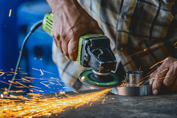 Closeup Grinder hand holding and Grindering the spare parts of metal over the wooden table in metal factory, industry concept