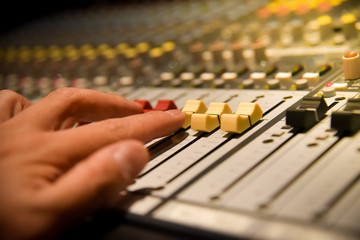 close-up hands of sound engineer adjusting audio mixer controller for live music and studio equipment. This is a quality audio system for professionals. vintage tone & effect light in control room.