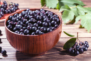 Ripe black chokeberry  in bowl and branch of aronia  on rustic wooden background