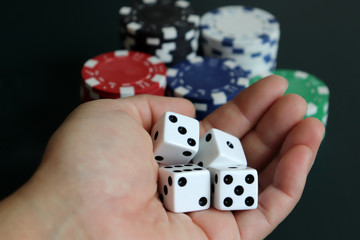 A woman's hand holding dice with a pile of casinos chips.