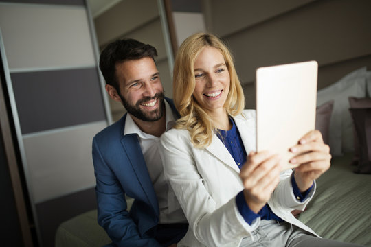 Businessman and businesswoman sitting on bed and using tablet