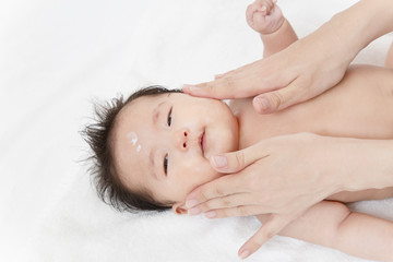 Fototapeta na wymiar 新生児の沐浴後の保湿方法を説明するマニュアル用写真。顔に保湿剤を両手の手の平でマッサージしながら塗るクローズアップ