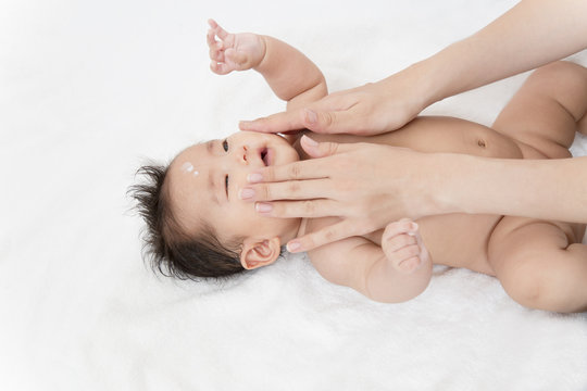 新生児の沐浴後の保湿方法を説明するマニュアル用写真。顔に保湿剤を両手の手の平でマッサージしながら塗るクローズアップ