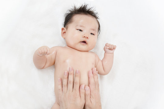 新生児の沐浴後の保湿方法を説明するマニュアル用写真。お腹と胸に保湿剤を両手の手の平でマッサージしながら塗るクローズアップ