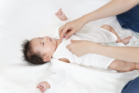 新生児の沐浴後に服を着せる方法を説明するマニュアル用写真、寝た赤ちゃんに白いロンパースを着せる手順イメージ