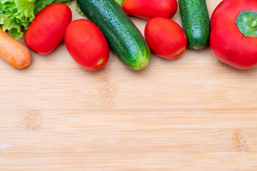 Vegetables on wooden cutting board. Vegetables: lettuce, onions, tomatoes, cucumbers, carrots, red sweet peppers.