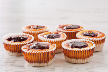 Seven delicious, homemade mini cheesecakes with berry jam in muffin cups on a wooden table