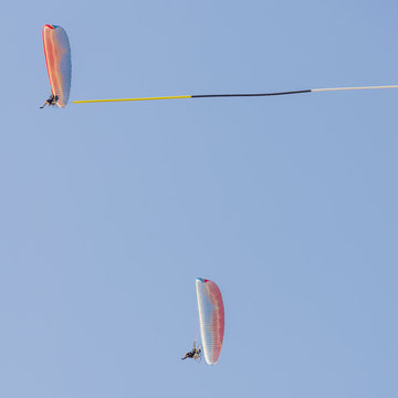 Pair of reckless pilots performs aerial acrobatics on board paramotors with the use of a banner against blue sky