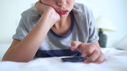 Close up view of funny healthy child with deformed skin and lips on face because of holding head with hand while using modern smartphone in bedroom at home. Real time full hd video footage.