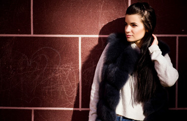 girl in a fur vest against a brick wall background