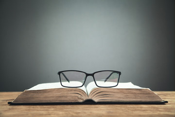 Open book and glasses on the wooden table.