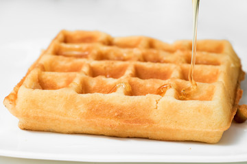 A pouring golden honey on fresh waffle, close up.