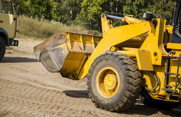 Tractor loader on the river bank performs the loading of gravel into the car body