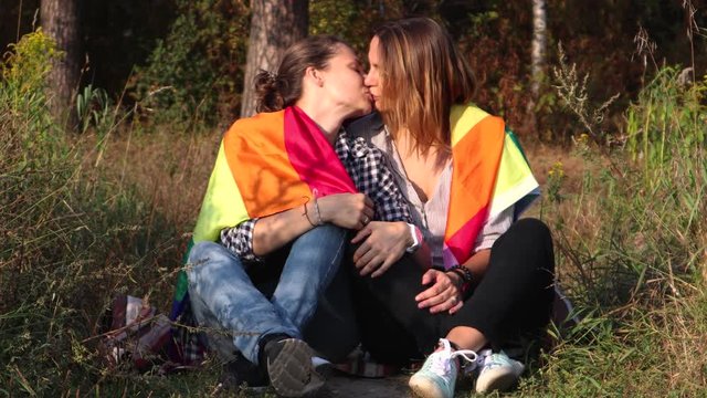 Two young women are sitting on a background of the rainbow flag. The sun is shining brightly, LGBT rights, lesbian family.