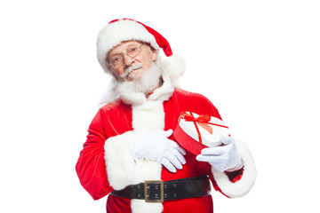 Christmas. Smiling Santa Claus in white gloves holds a red and white heart-shaped gift box with a red ribbon. Isolated on white background.