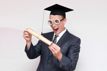 Graduate student in the cap holding in hands a diploma scroll isolated on gray background. Education concept.