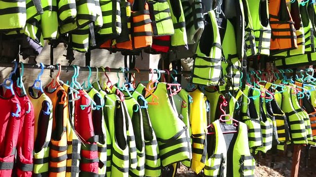Many colorful life vests of yellow, orange, green and red colors hanging outdoor on sunny summer day. Real time full hd video footage.