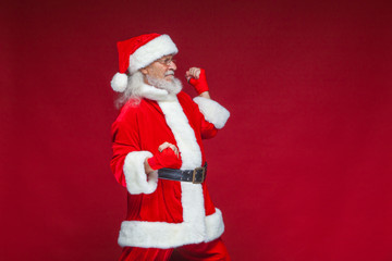 Christmas. Santa Claus with red bandages wound on his hands for boxing imitates kicks. Kickboxing, karate, boxing. Isolated on red background.