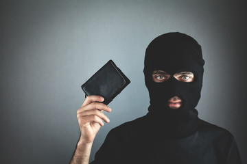 Thief in black mask holding wallet and looking at camera.